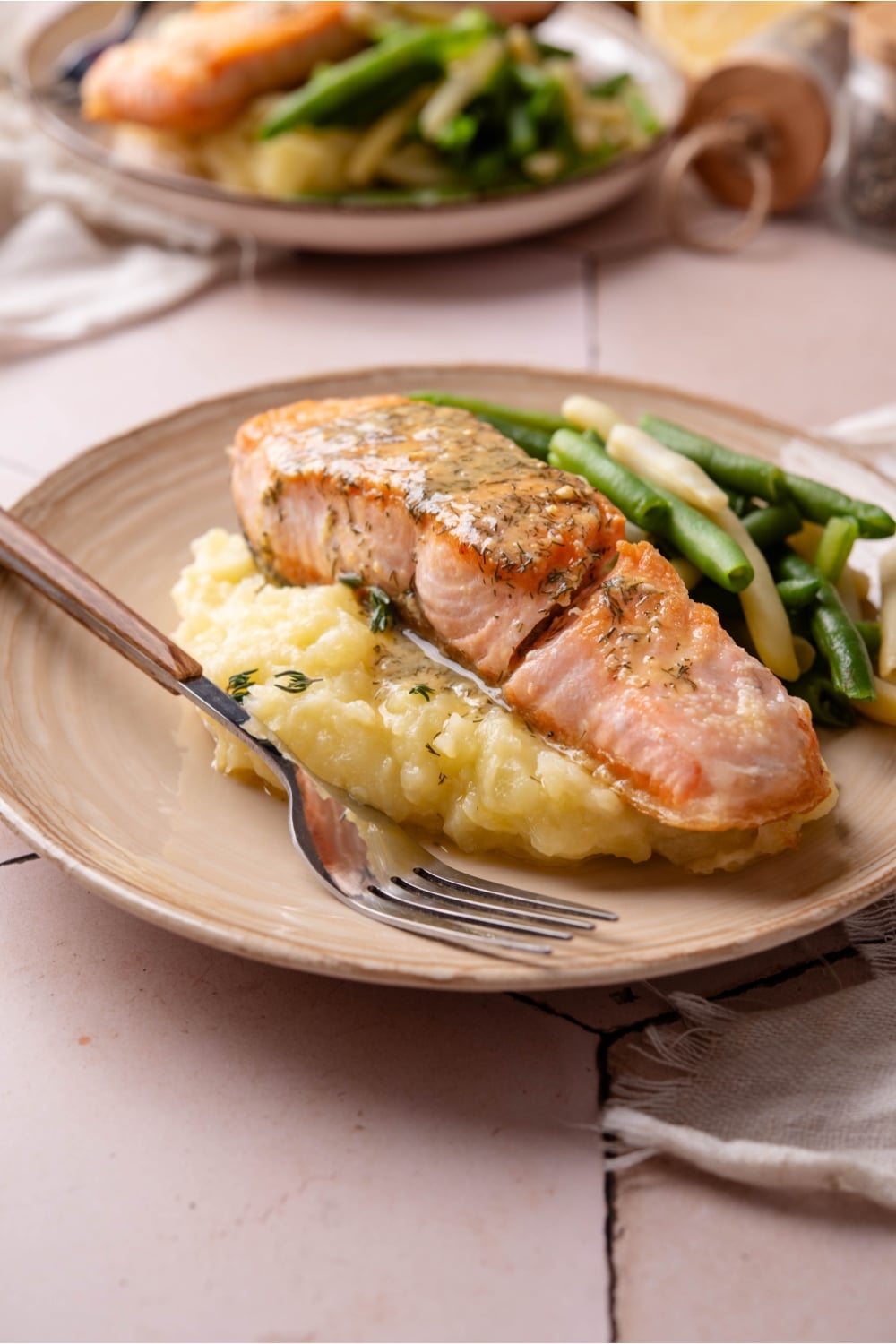 A salmon fillet on mashed potatoes on a white plate with a fork next to it.