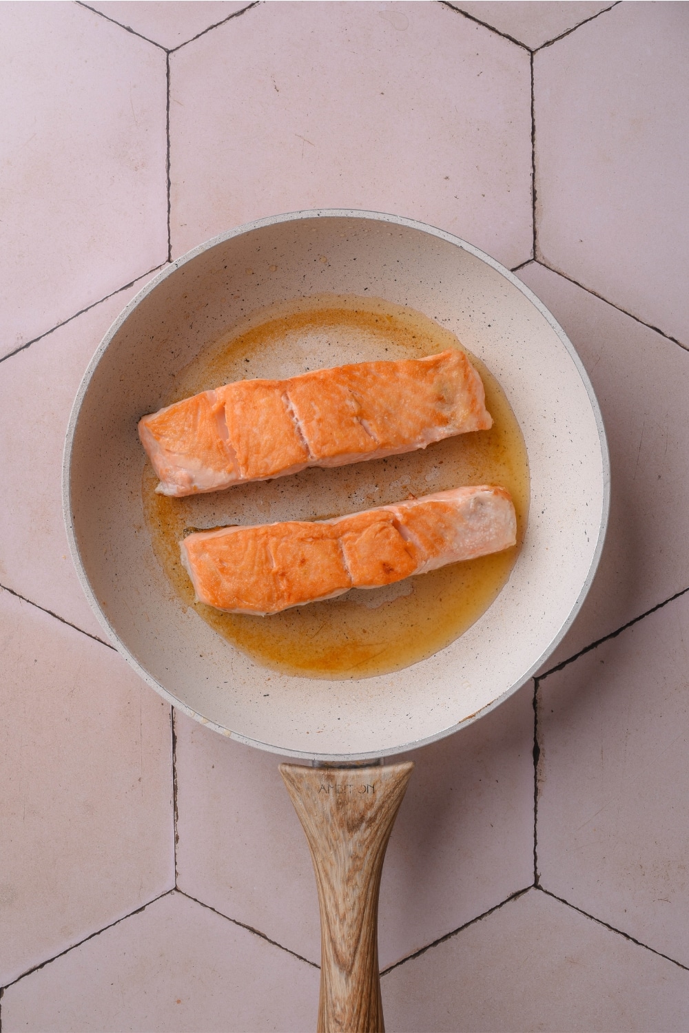 Two pieces of salmon in a frying pan on a white counter.