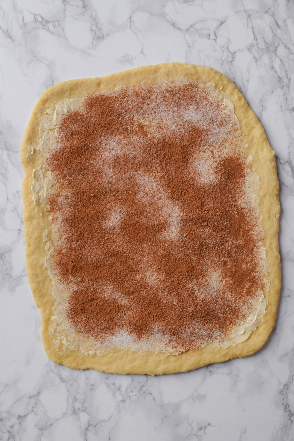 Rolled out dough topped with cinnamon roll filling.