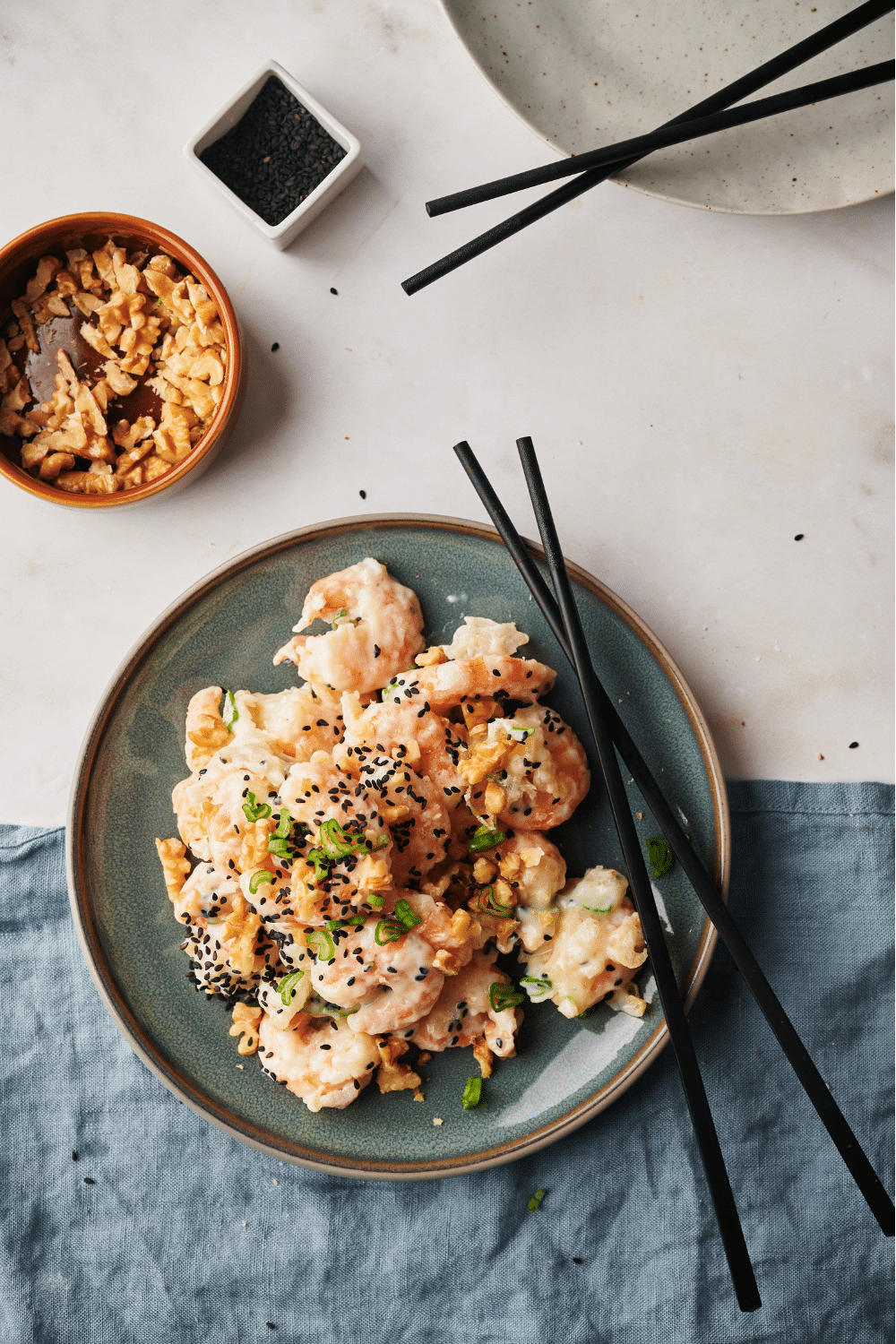 A plate of honey walnut shrimp garnished with sesame seeds, sliced green onions, and walnuts. A set of chopsticks is on the plate.