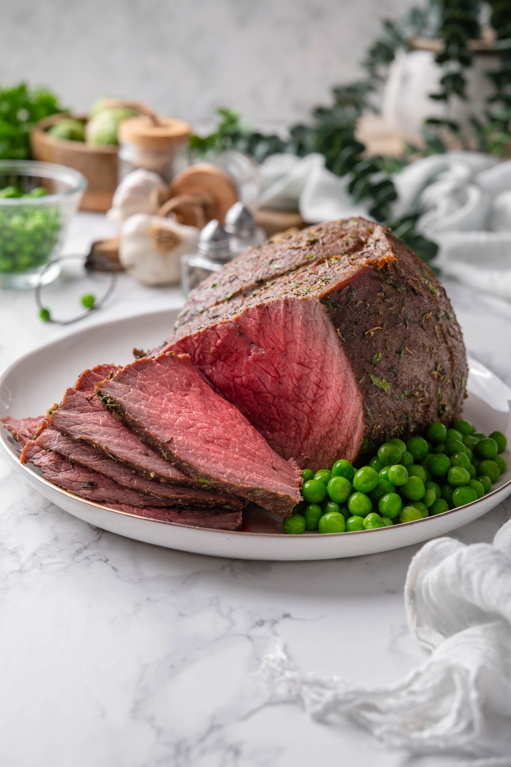 Medium rare sirloin tip roast cut into thin slices and served on a plate with green peas.