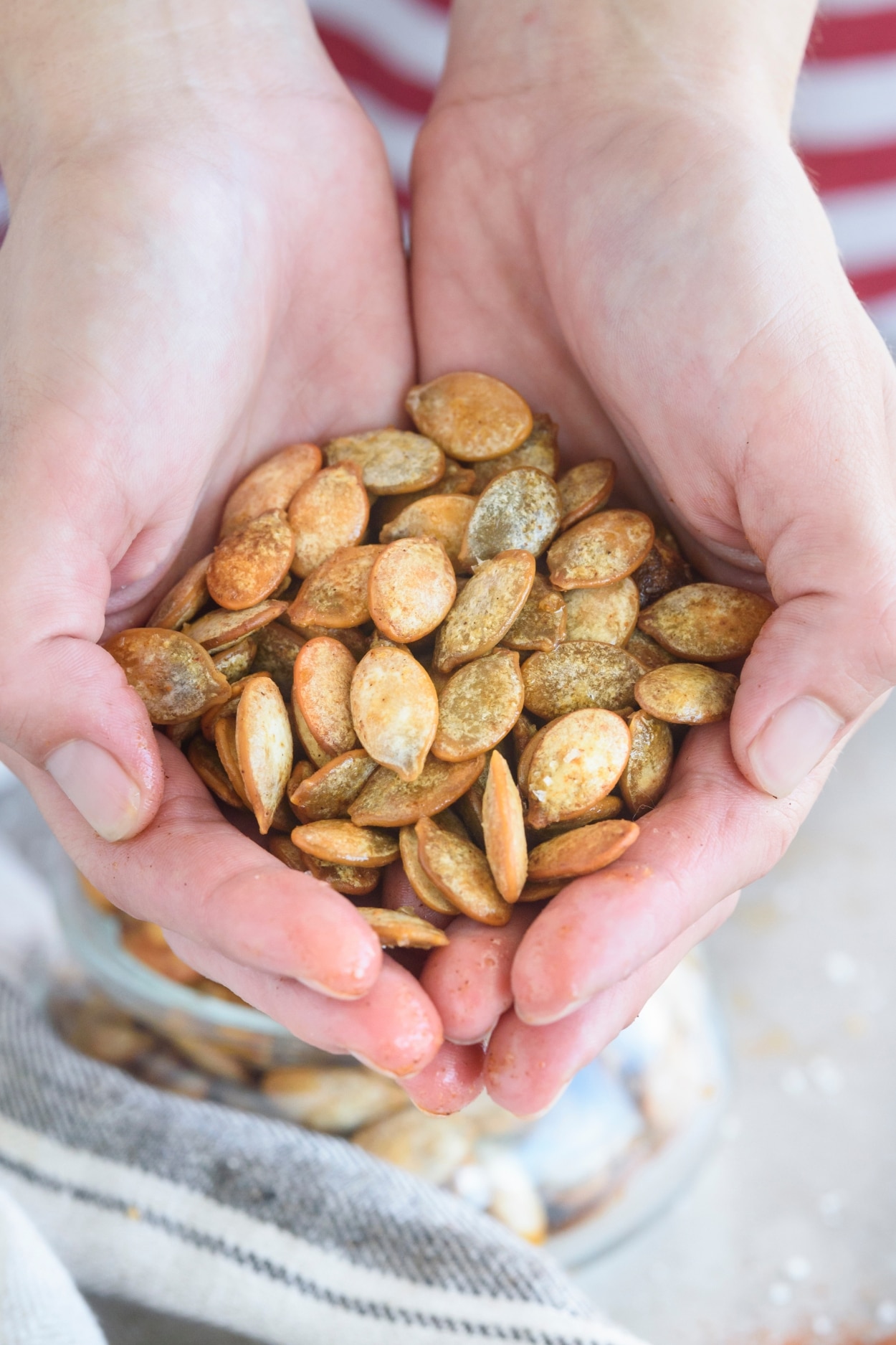 Two hands holding a bunch of pumpkin seeds.