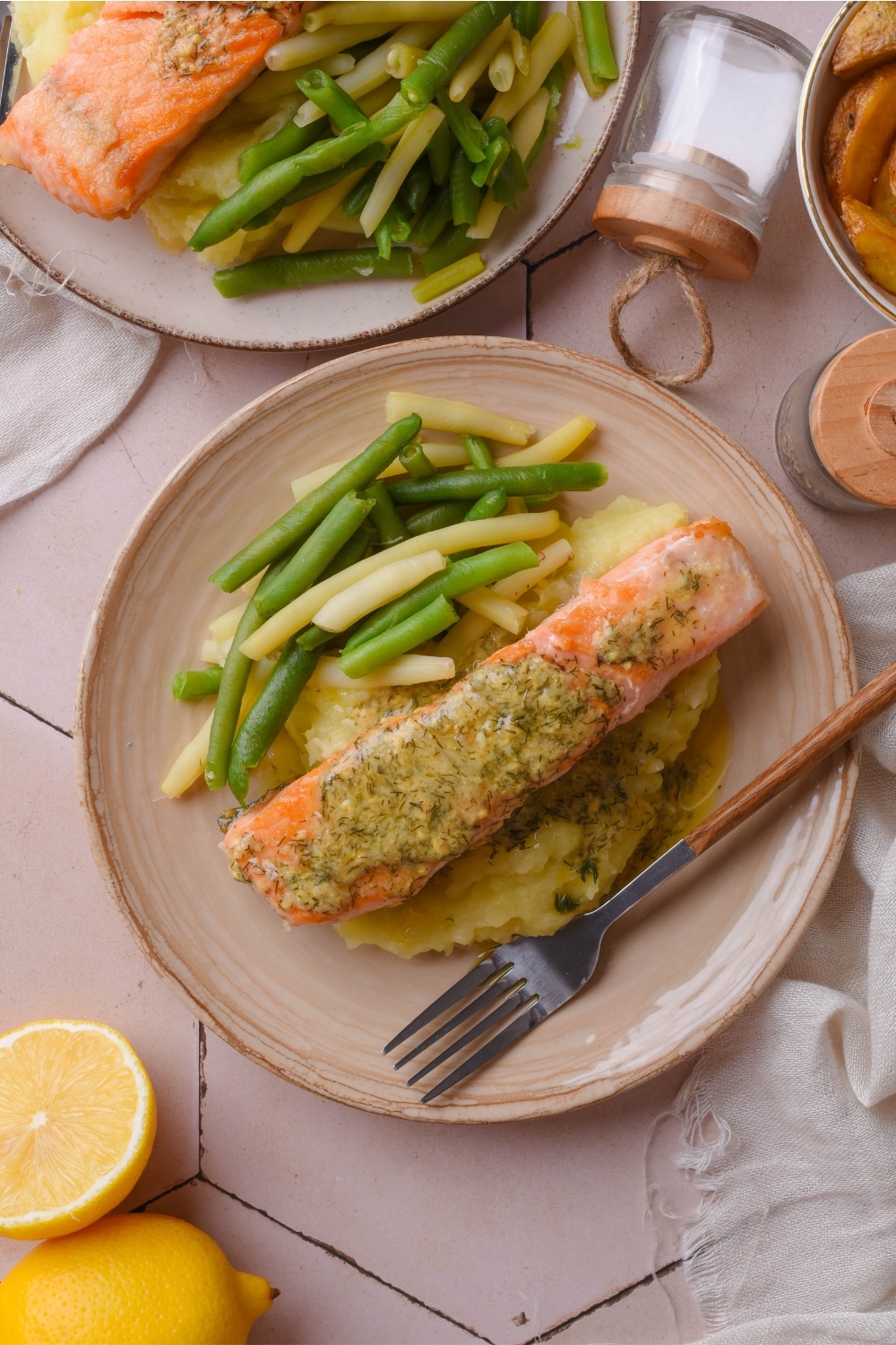 A lemon garlic dill sauce on mashed potatoes on top of a plate. Next to the salmon are green beans.