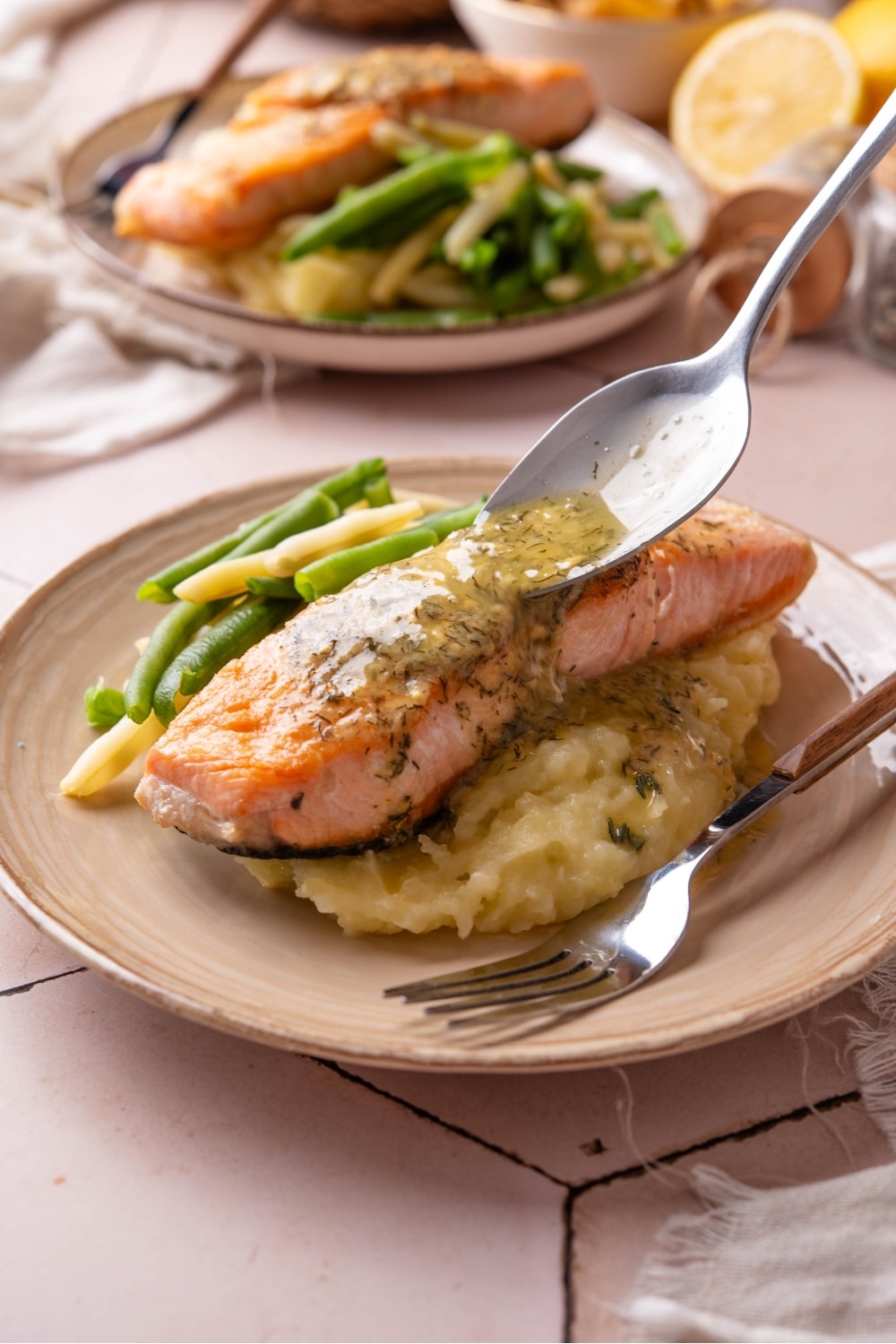 A spoon drizzling a lemon butter sauce on top of a piece of salmon on mashed potatoes on a plate.