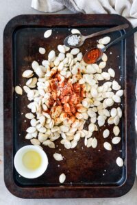 Cayenne pepper and salt on top of pumpkin seeds on a baking sheet.