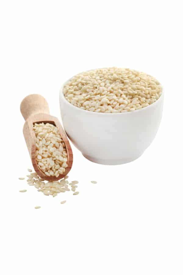 A bowl of sesame seeds and a woodedn spoon filled with sesame seeds.