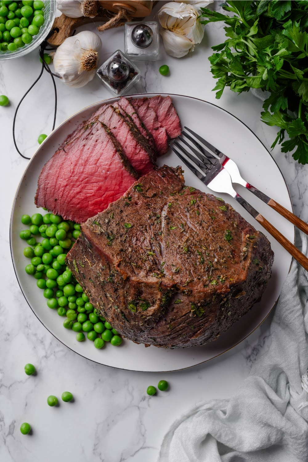 An overhead view of a plate of medium rare sirloin tip roast, sliced and served with green peas and two forks.