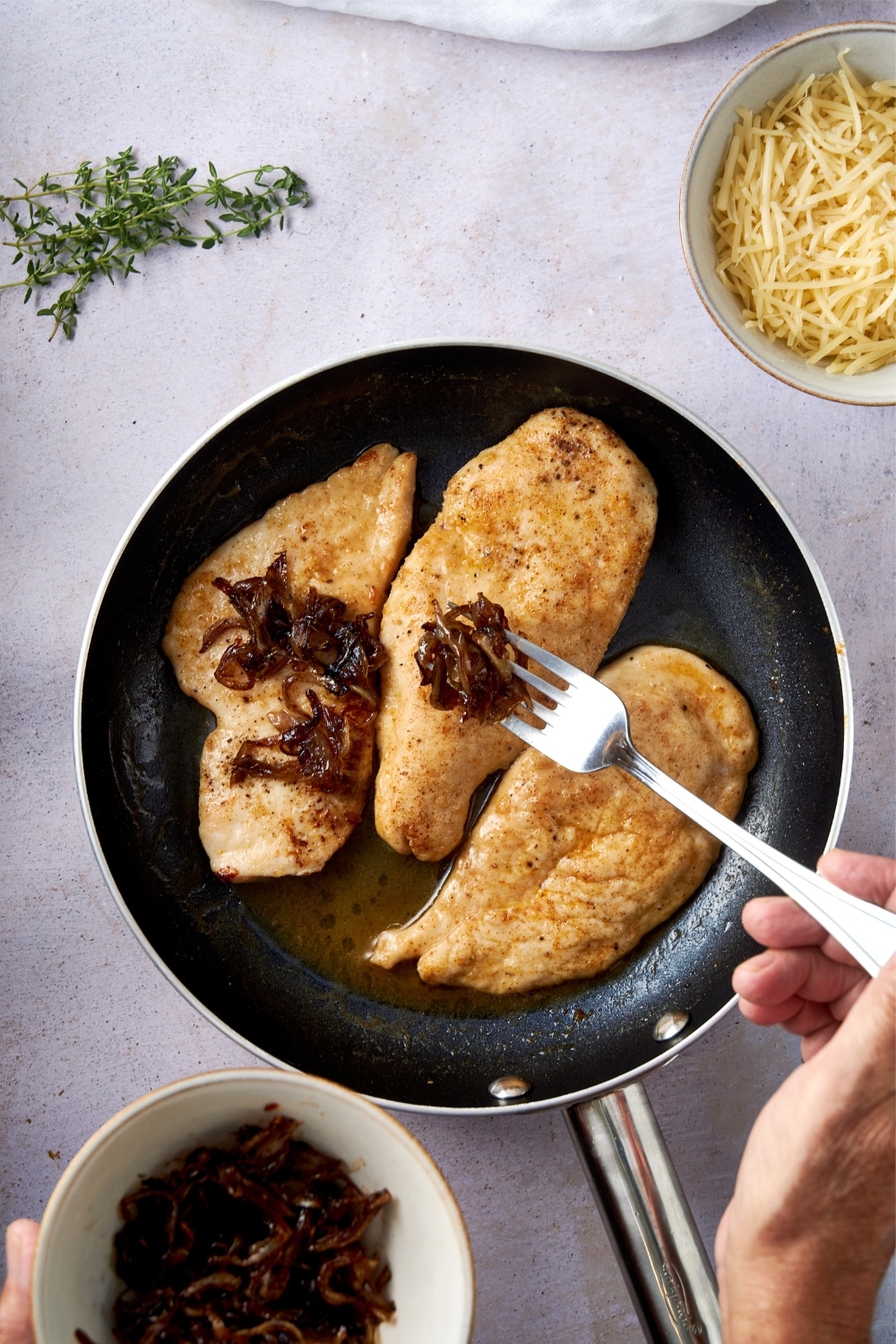 Placing caramalized onions on top of chicken cutlets in a skillet with a fork.