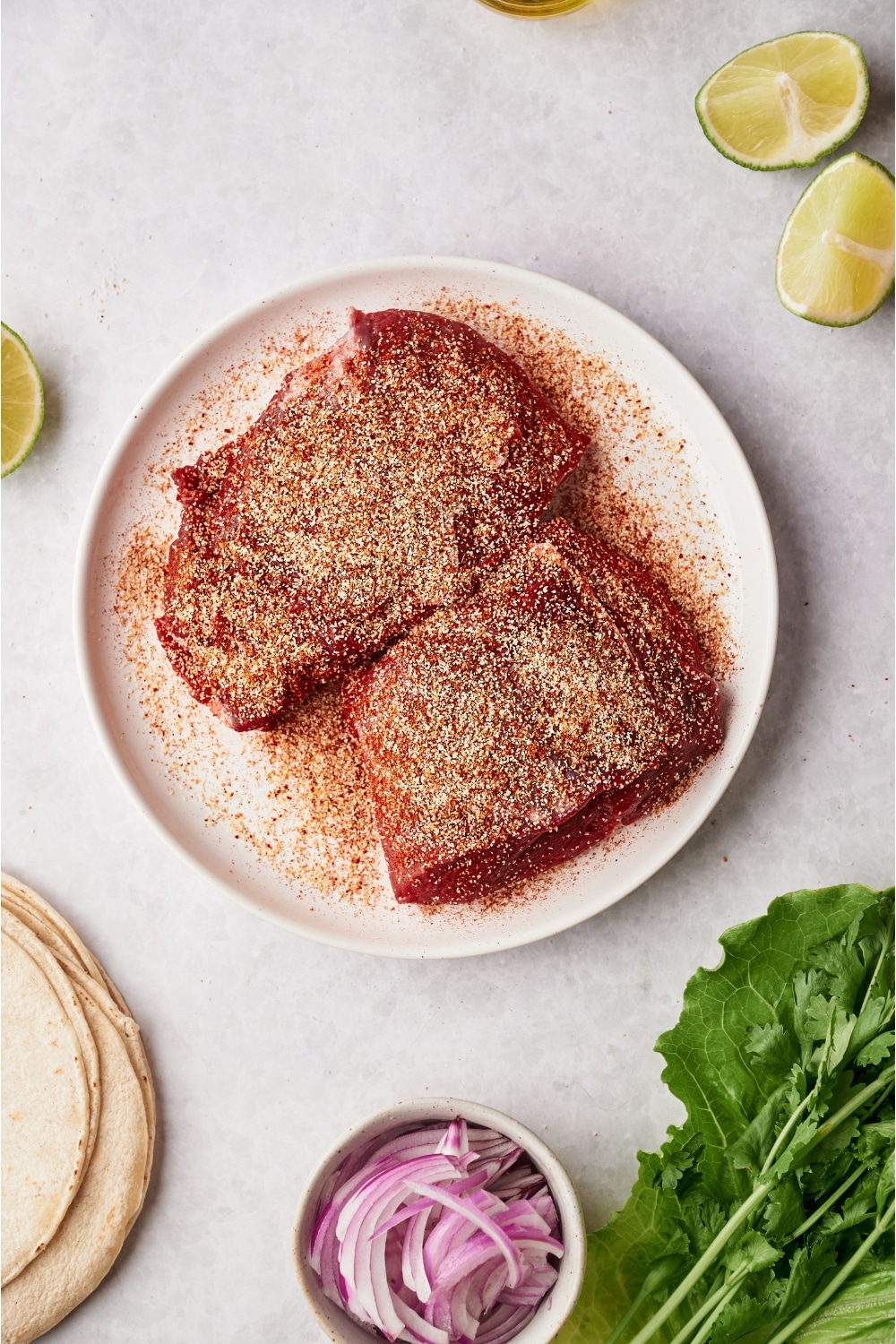 Seasoning on top of two flank steaks on a plate.