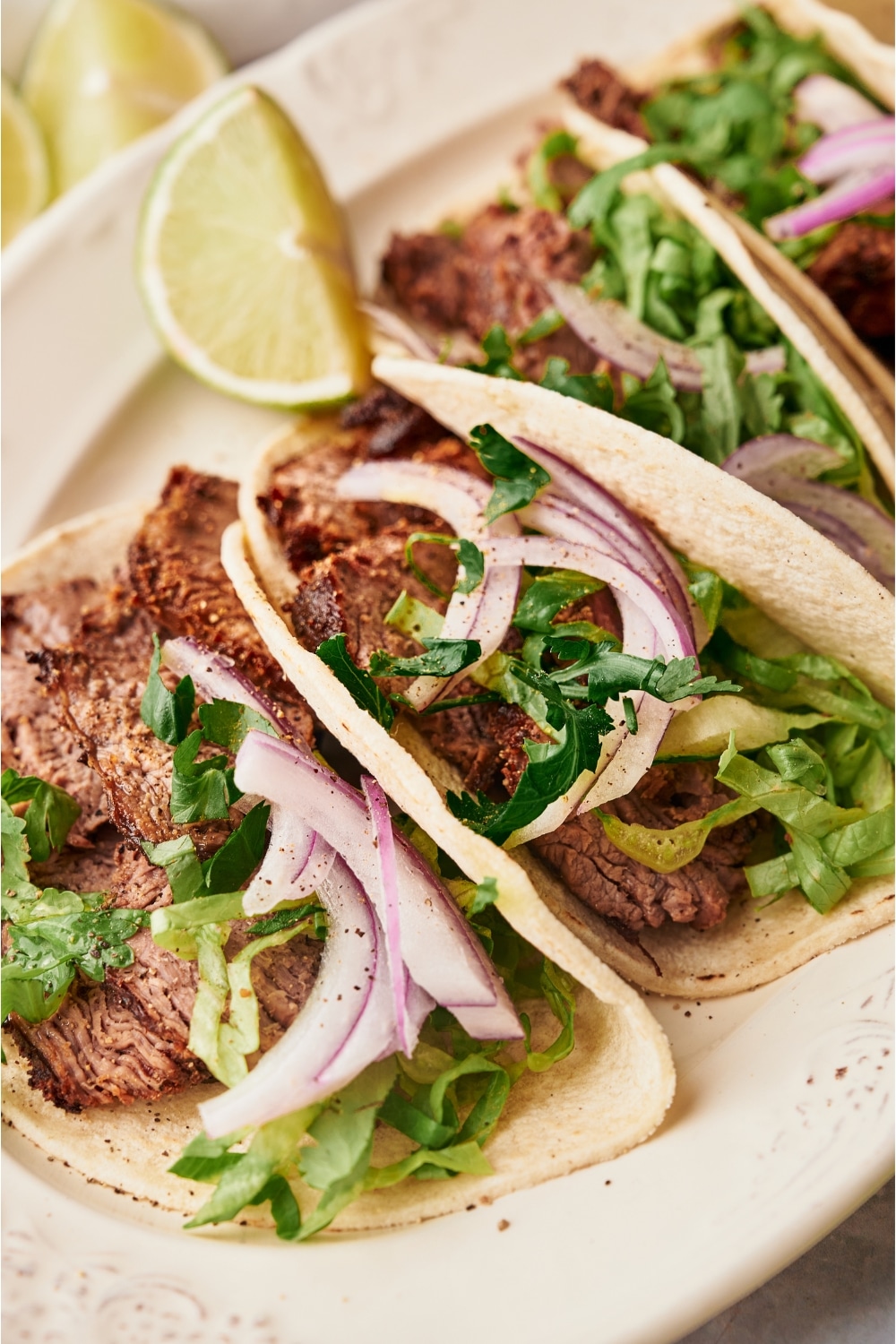 Two steak tacos with red onion and cilantro in them on a white plate.