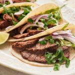 Steak, red onion, and cilantro in a flour tortilla. Behind it are a few more steak tacos.