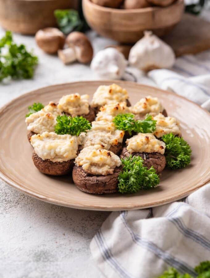 A couple of cream cheese stuffed mushrooms on a plate that is on a grey counter.