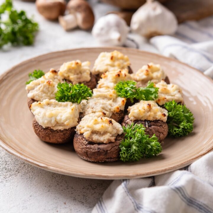 A couple of cream cheese stuffed mushrooms on a plate that is on a grey counter.