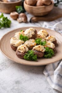 A plate filled with cream cheese stuffed mushrooms. The plate is on a grey counter.