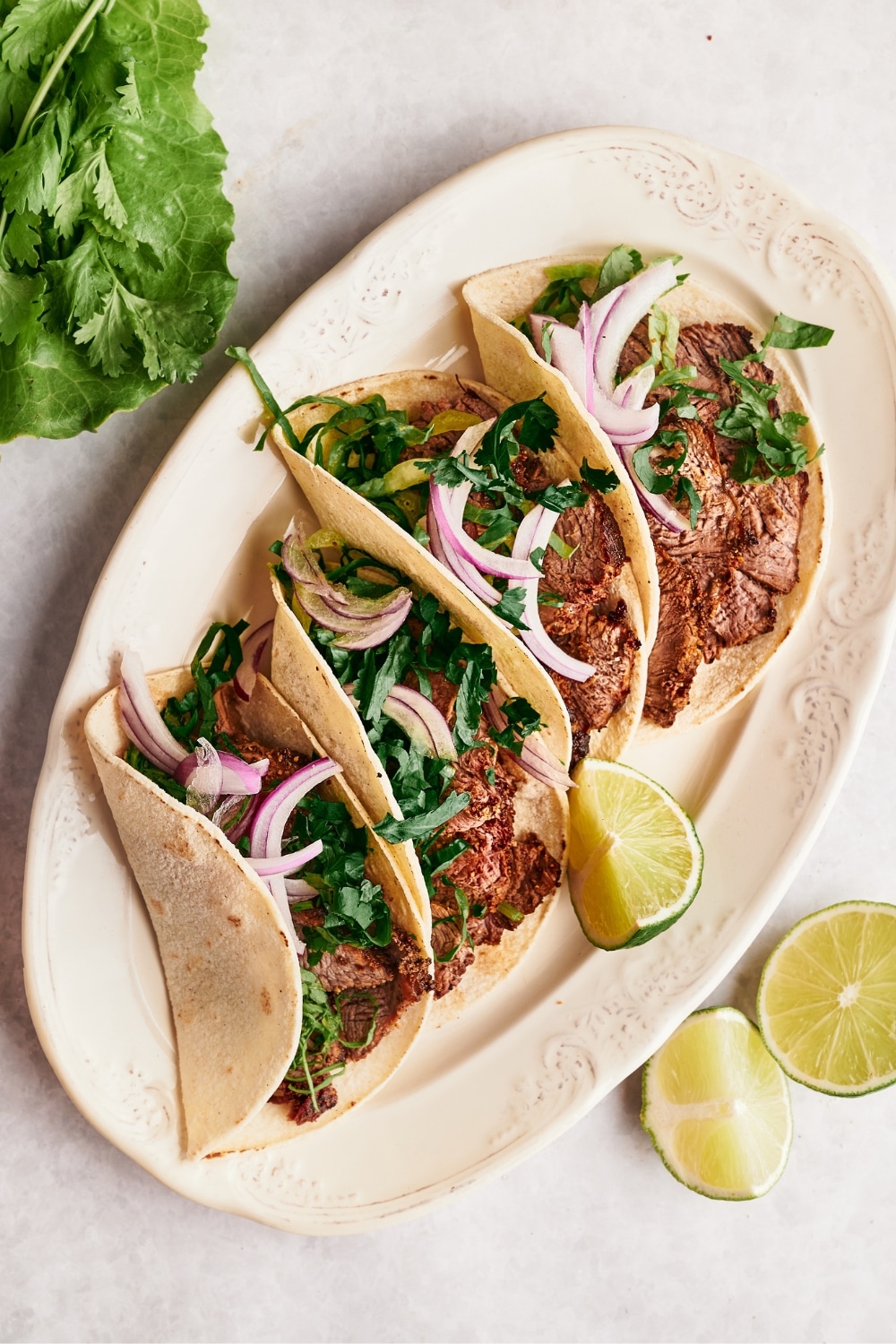 Four steak tacos with red onion and cilantro on a white plate.