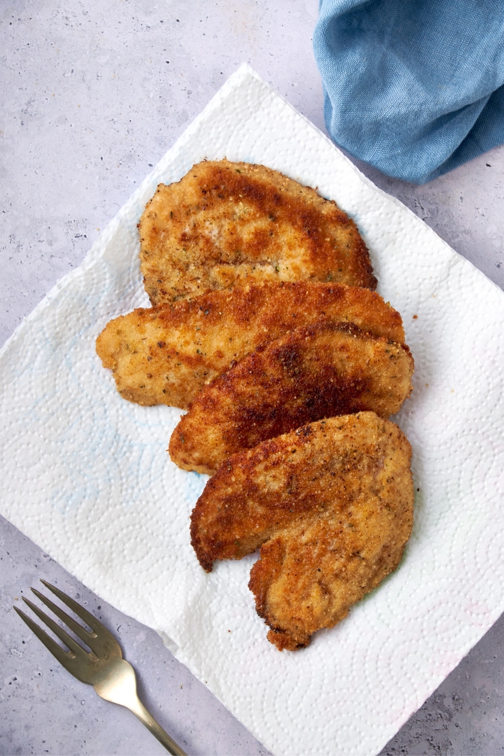 Four cooked turkey cutlets on a paper towel-lined plate with a fork.