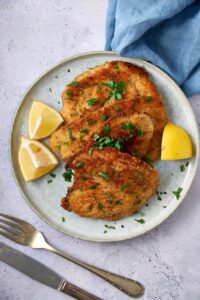 Turkey cutlets on a plate garnished with fresh herbs and lemon wedges.