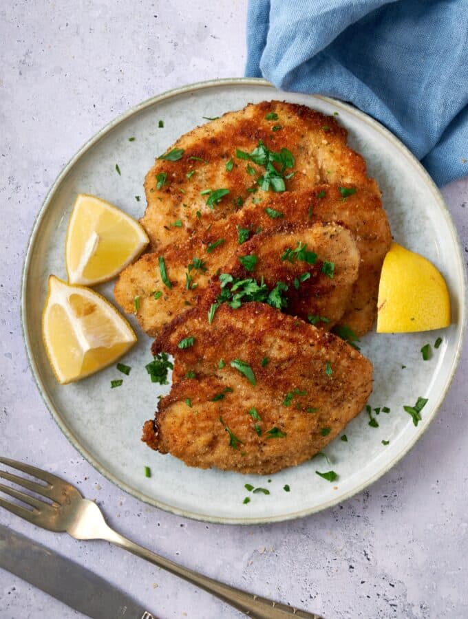 Turkey cutlets on a plate garnished with fresh herbs and lemon wedges.