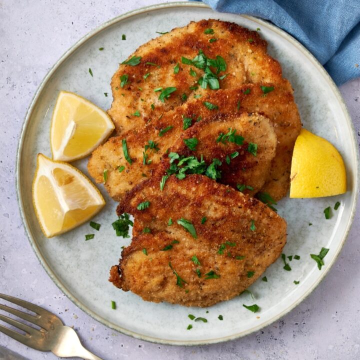 Turkey cutlets on a plate garnished with fresh herbs and lemon wedges.