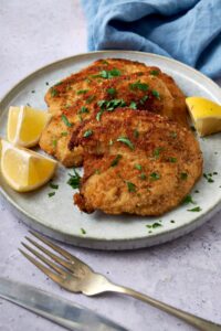A plate of turkey cutlets garnished with fresh herbs and lemon wedges.