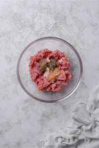 A glass bowl of ground turkey with minced garlic, brown sugar, and dried herbs.