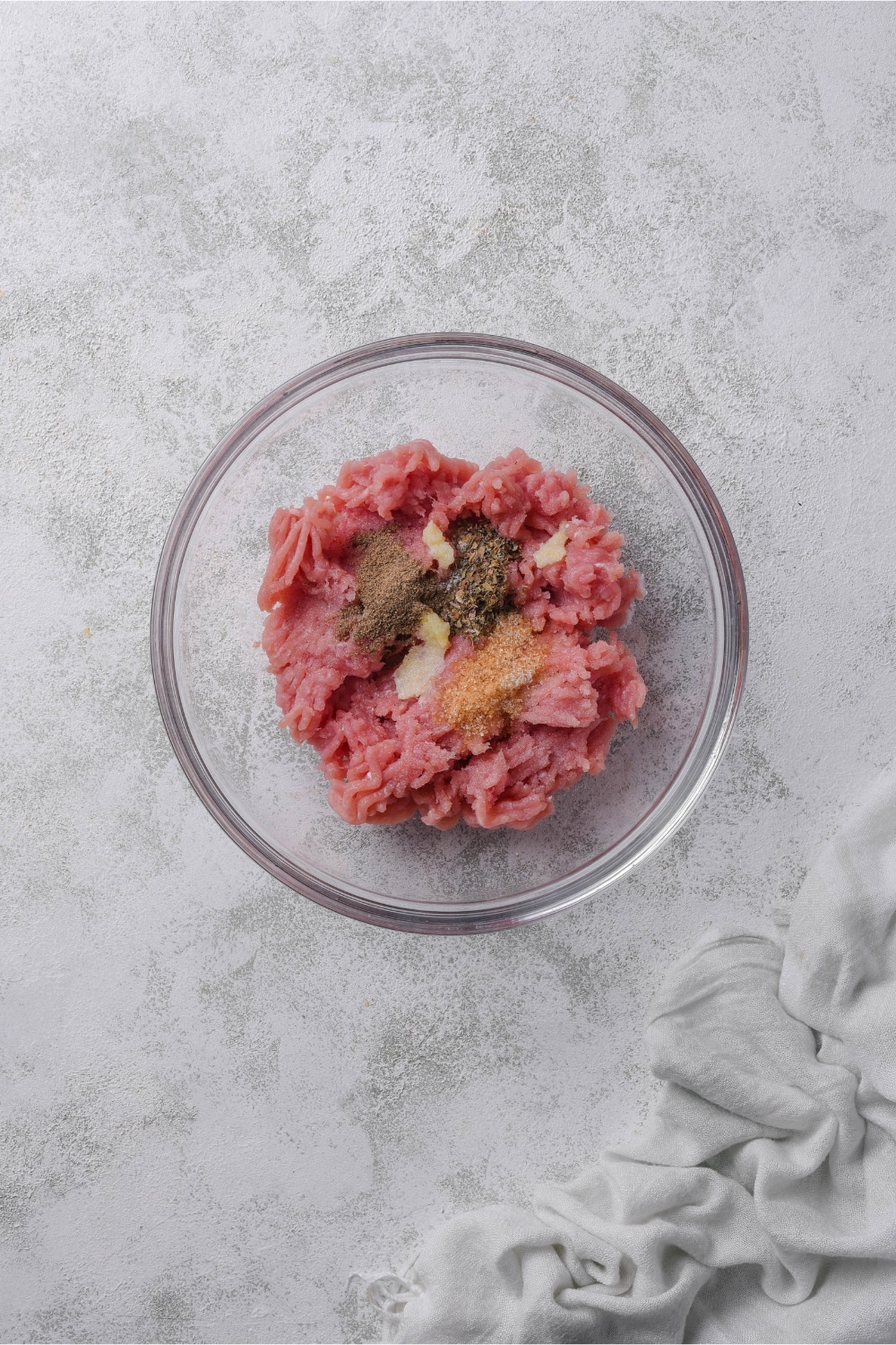 A glass bowl of ground turkey with minced garlic, brown sugar, and dried herbs.