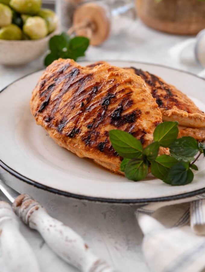 Grilled yogurt-marinated chicken breasts on a white plate, garnished with fresh herbs.