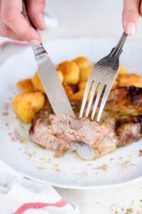 A fork and knife holding a bite of cooked pork chop.