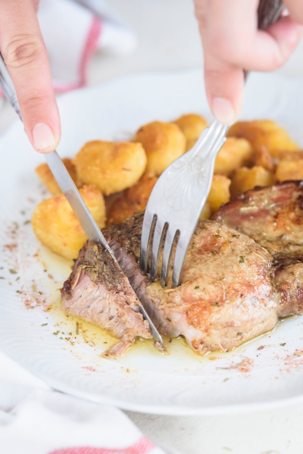 A person using a fork and knife to cut a piece of pork chop.