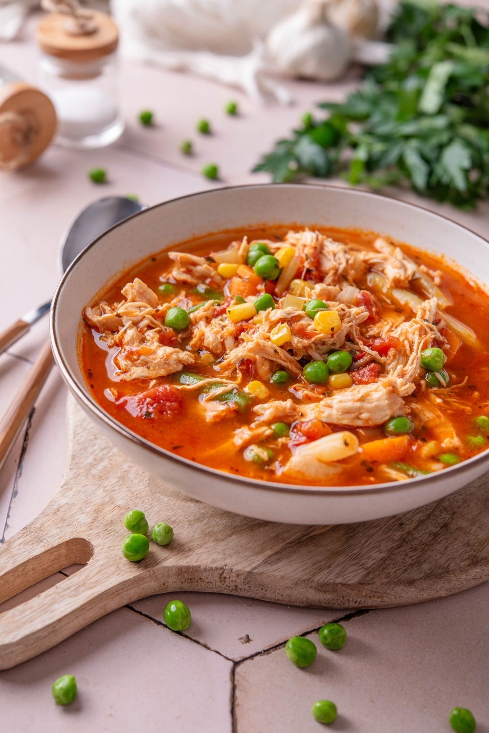 A bowl of soup with tomatoes, shredded chicken, peas, corns, and carrots.