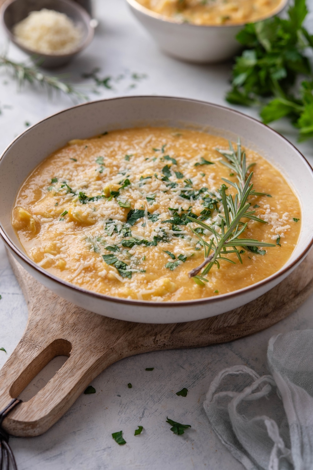 A bowl of chickpea soup with kale and parmesan cheese on top and garnished with fresh rosemary.