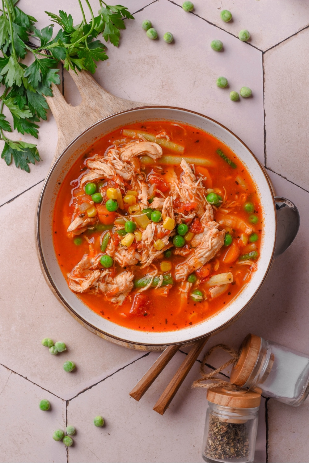 Overhead view of a bowl of soup with shredded chicken, peas, corn, and green beans in a tomato broth.