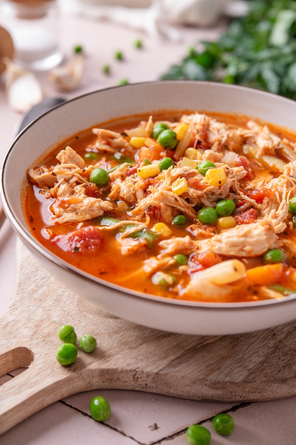 A bowl of soup with tomatoes, shredded chicken, peas, corns, and carrots.