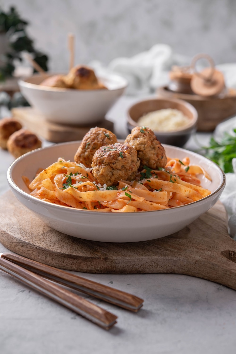 A plate of pasta in red sauce with three meatballs on top. The plate is on a wooden board next to a set of silverware.