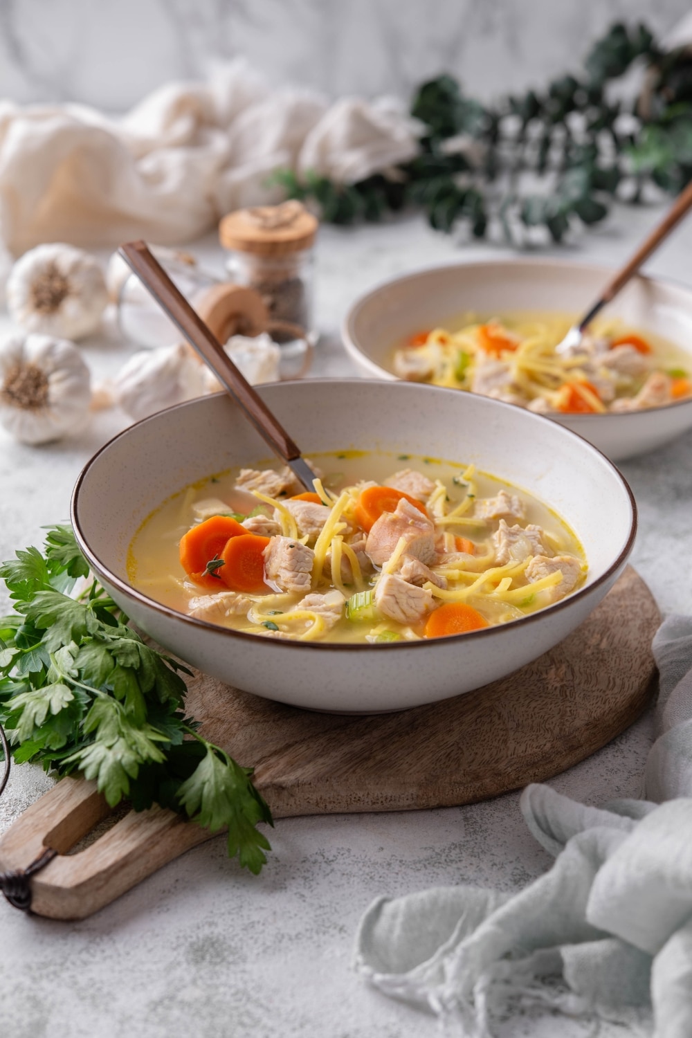 A bowl of turkey noodle soup with chunks of carrots and celery. There is a spoon in the bowl and a second bowl in the background.