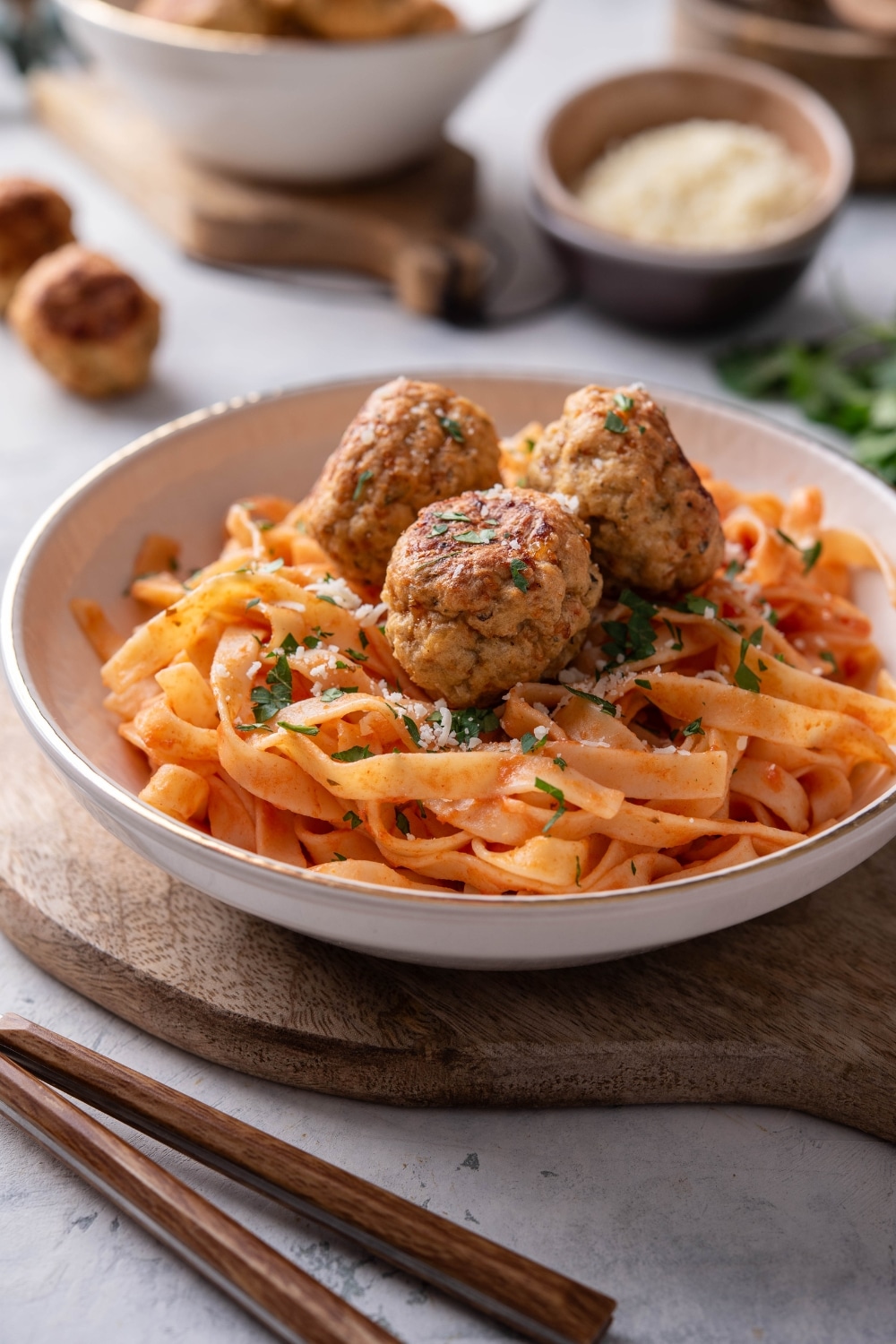 A plate of pasta in red sauce with three meatballs on top. The plate is on a wooden board next to a set of silverware.