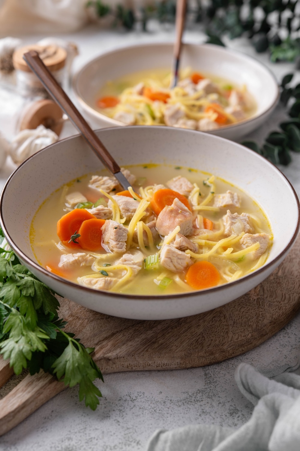 A bowl of turkey noodle soup with chunks of carrots and celery. There is a spoon in the bowl and a second bowl in the background.