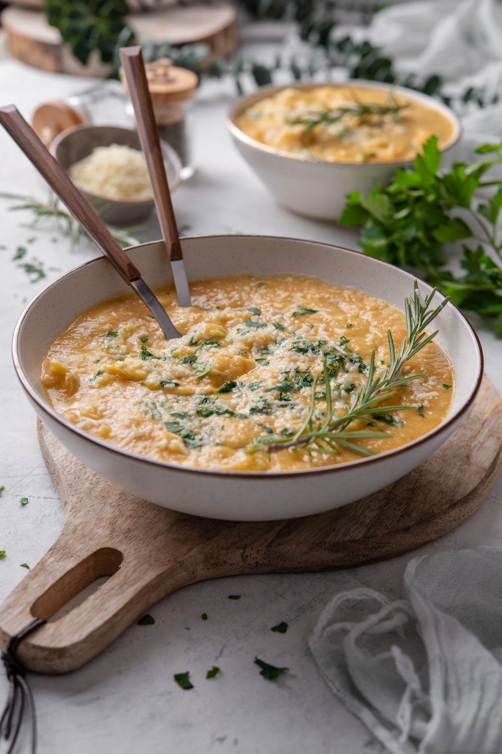 A bowl of chickpea soup with kale, parmesan cheese, and rosemary on top. Two spoons are in the bowl.