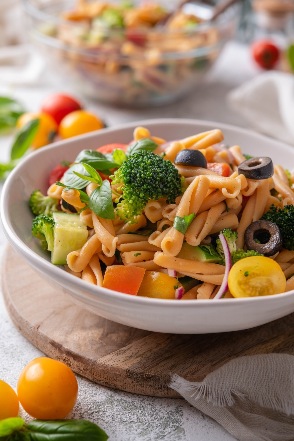 A bowl of pasta salad with black olives, cherry tomatoes, fresh herbs, cucumber, black olives, and broccoli florets.