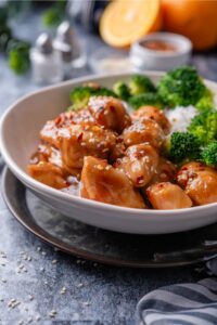 A plate of orange chicken garnished with sesame seeds and sides of broccoli and white rice.