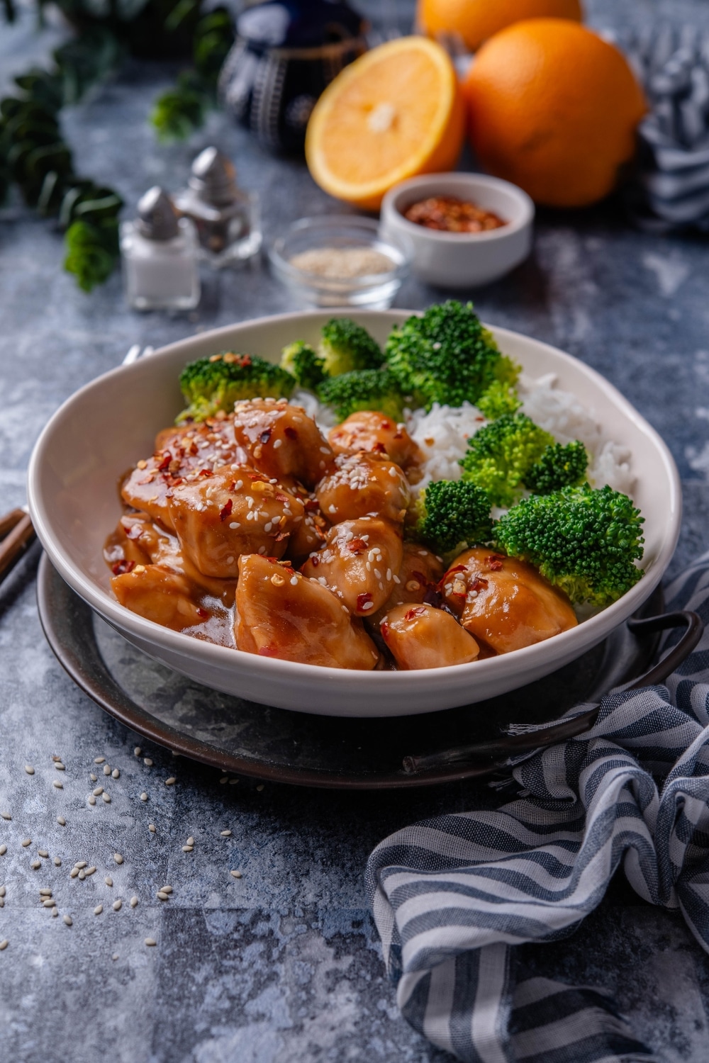 A plate of orange chicken garnished with sesame seeds and sides of broccoli and white rice.