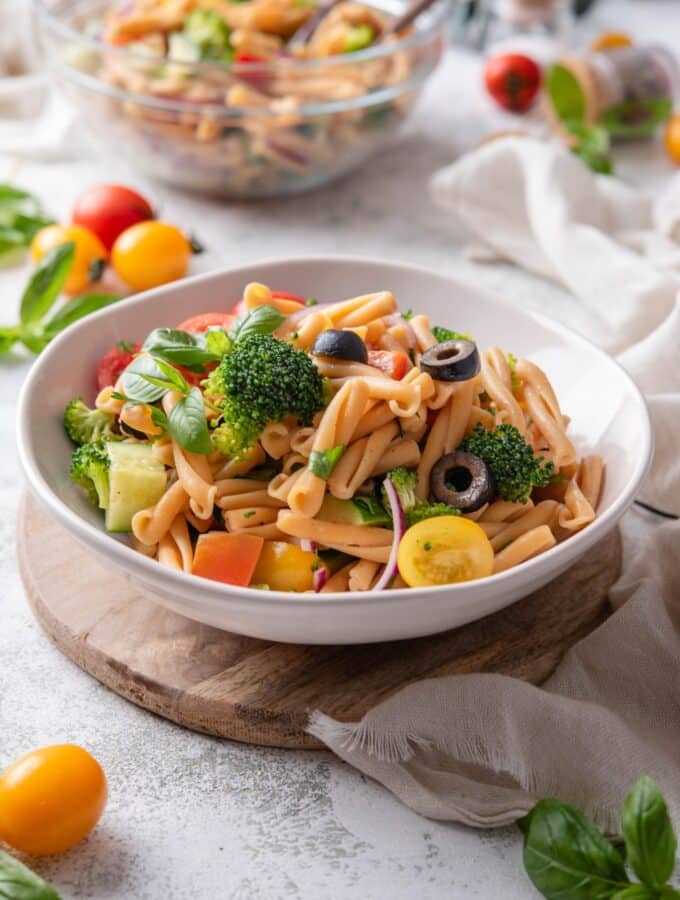 A bowl of pasta salad with black olives, cherry tomatoes, fresh herbs, cucumber, black olives, and broccoli florets.