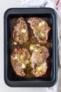 A baking dish filled with cooked pork chops covered in melted butter.