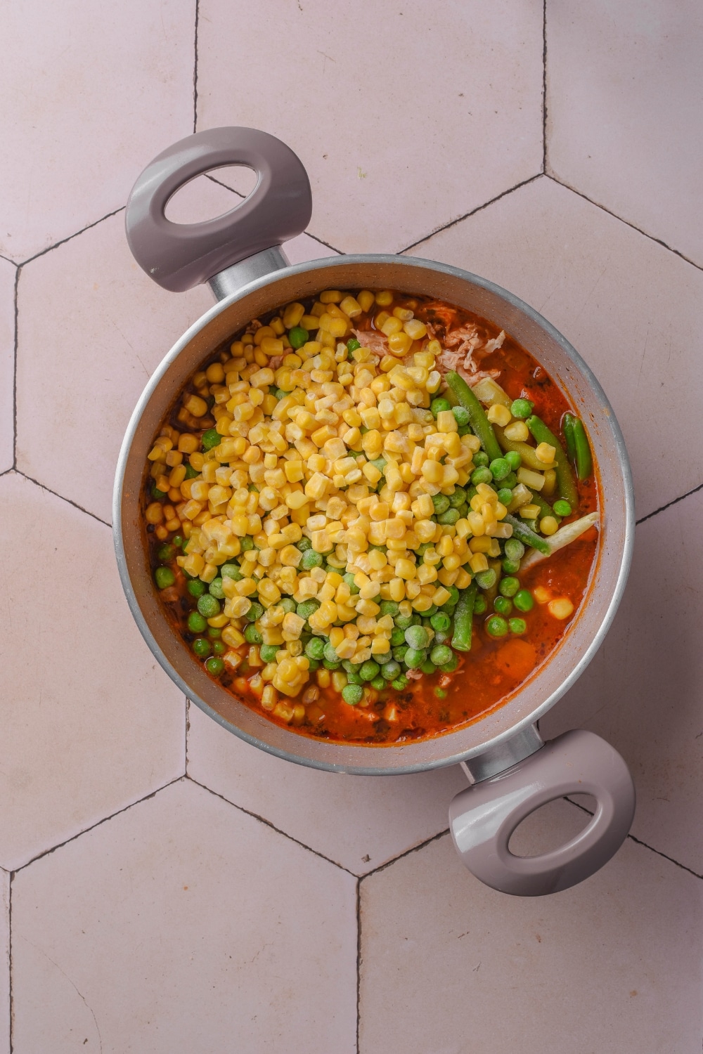 A pot filled with corn, green beans, and peas in a tomato broth.