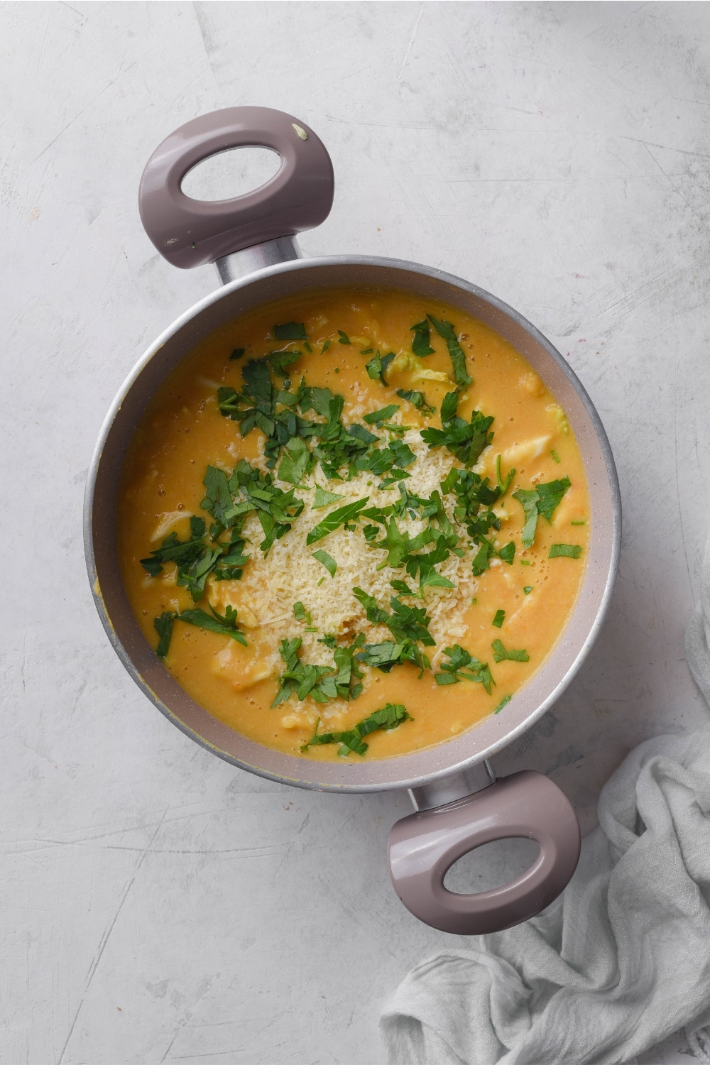 A pot filled with soup with chopped kale and parmesan cheese.