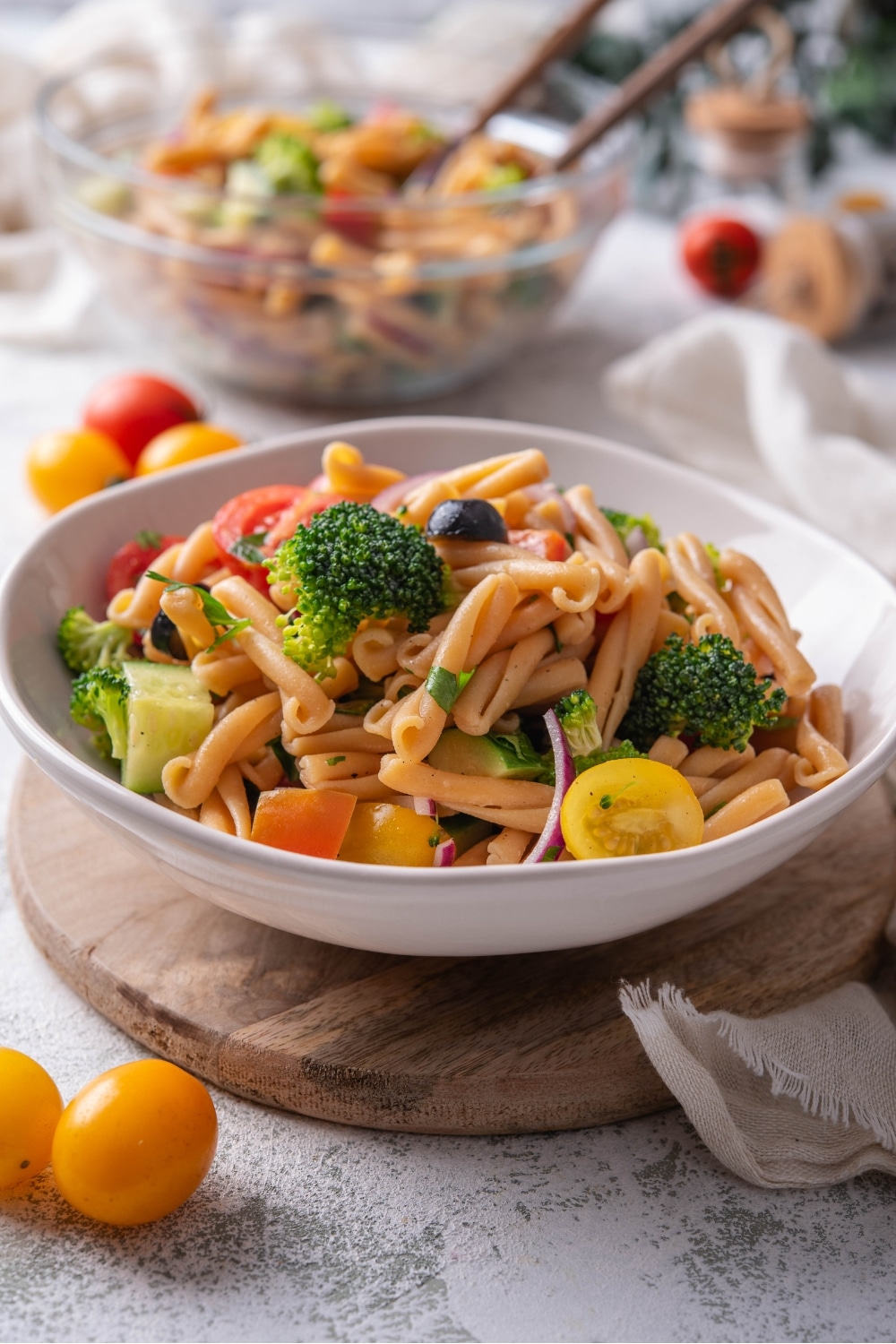 A bowl of pasta salad with black olives, cherry tomatoes, fresh herbs, cucumber, black olives, and broccoli florets.