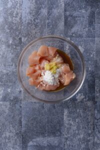 A bowl of raw chicken pieces with minced ginger, soy sauce, and baking soda.
