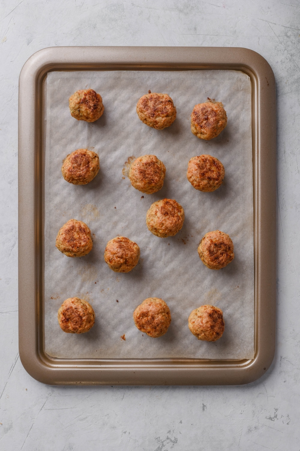 Thirteen baked meatballs on a baking sheet lined with parchment paper.