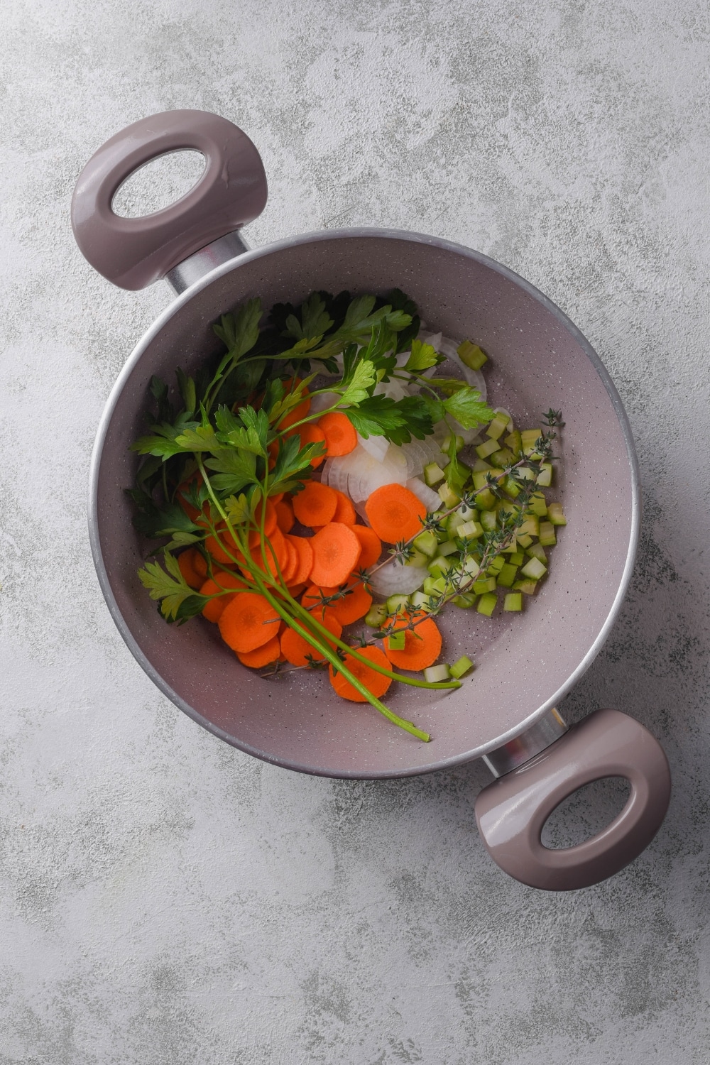 A pot filled with fresh herbs, onion, carrots, and celery.