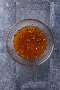 A bowl of orange sauce with red pepper flakes.